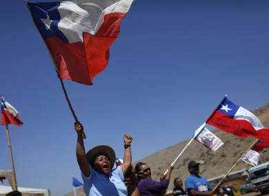 Relatives of trapped miners wave Chilean flags as they welcome vehicles transporting containers to be used as a health center