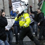 A motorbike police officer holds back Sinn Fein protesters who broke through the gates at government buildings. (AP Photo/Peter Morrison)