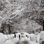 People clear their cars while other cars make their way slowly through the streets of New York, which has experienced its snowiest January on record.