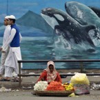 An Indian street flower vendor sets up for the day on a pavement in Bangalore in front of a dolphin mural which is part of city's beautification drive.