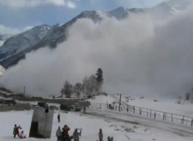 Snowboarders at the base of the mountain film the avalanche
