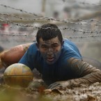 A competitor pushes a rugby ball as he crawls under barbed wire. (AP Photo/Jon Super/PA Images)