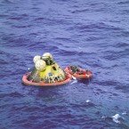 The three astronauts inside their landing pod after returning through the Earth's atmosphere. Members of the US Navy are alongside in a raft. (NASA)